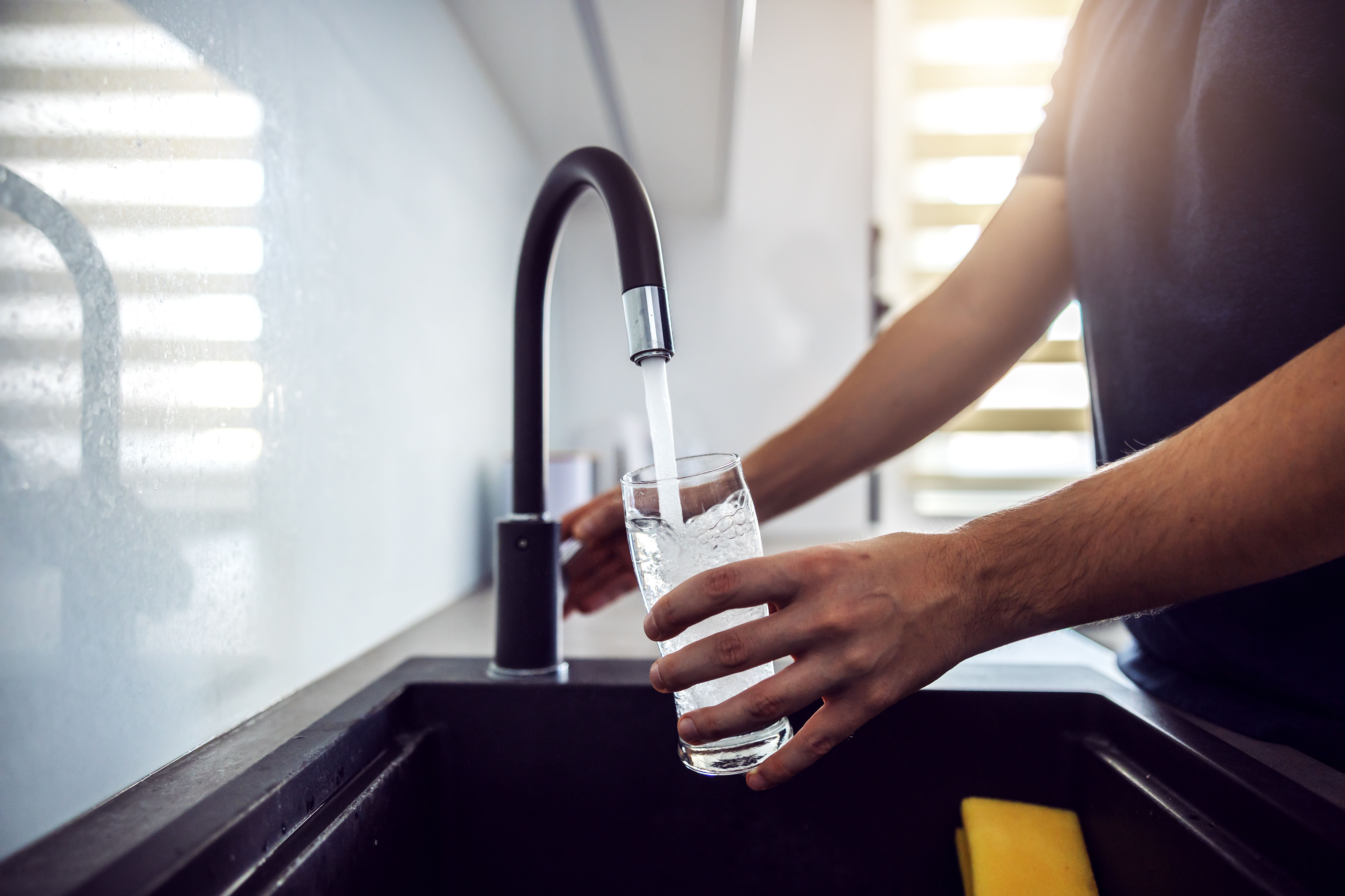 Close up of young man pouring fresh water from kitchen sink. Home interior - Dusan Petkovic - stock.adobe.com