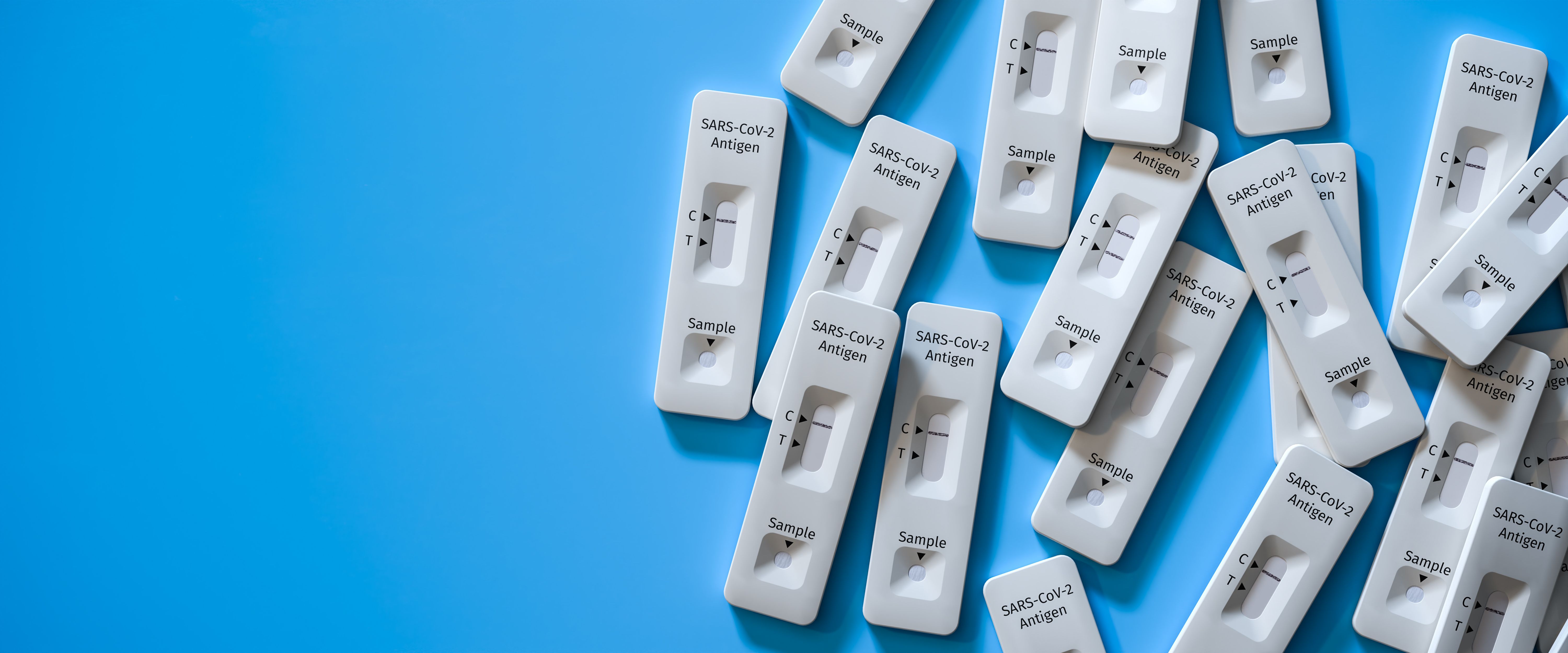 Mass testing for Covid-19 / SARS-CoV-2 infection concept: Several rapid antigen test kits. One kit in the middle showing a positive result (two lines visible) | Image Credit: Andreas Prott - stock.adobe.com