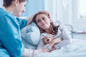 mother rubbing her daughters head as she holds a teddy bear in a hospital bed