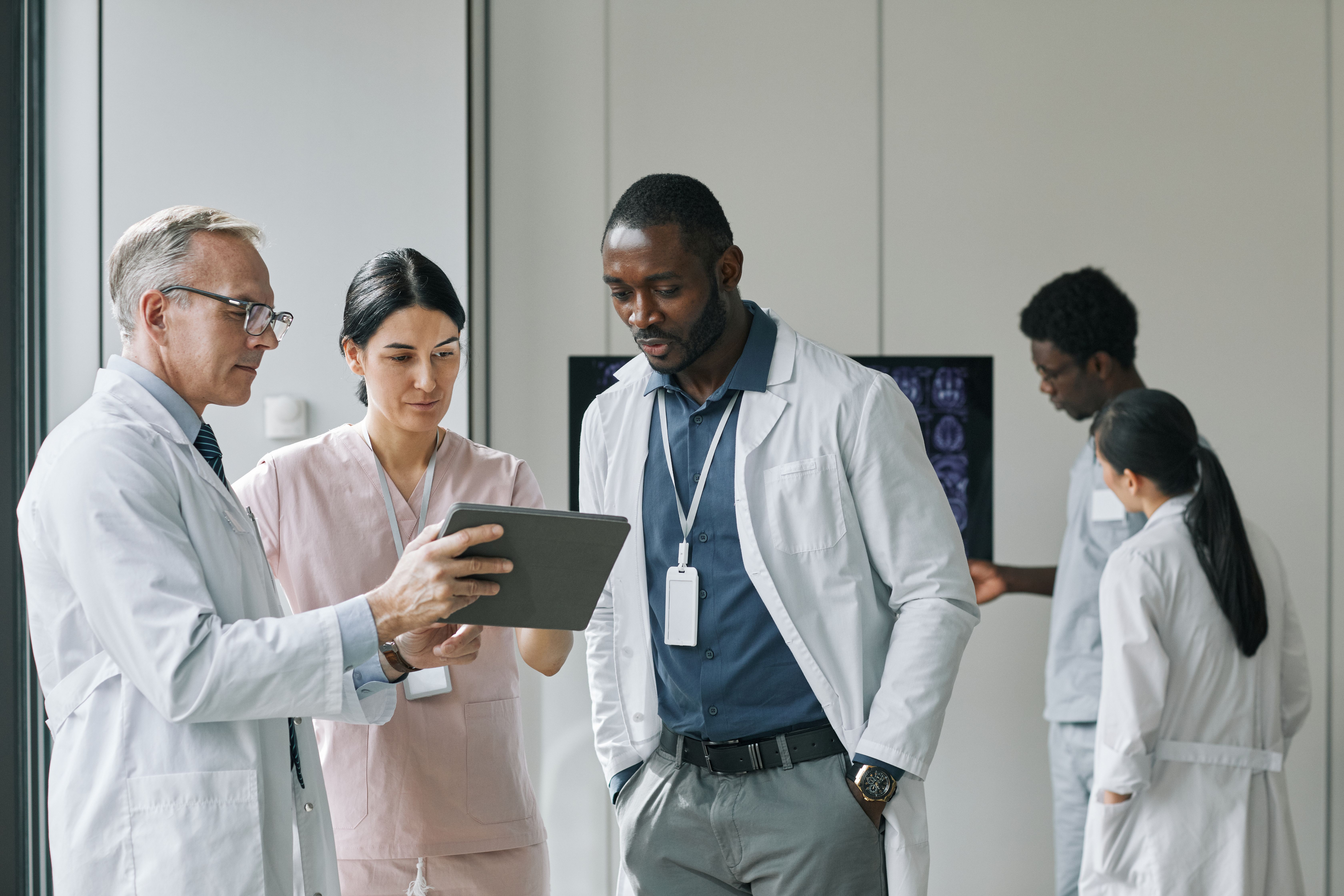 Group of doctors talking and looking at tablet | Image credit: Seventyfour – stock.adobe.com