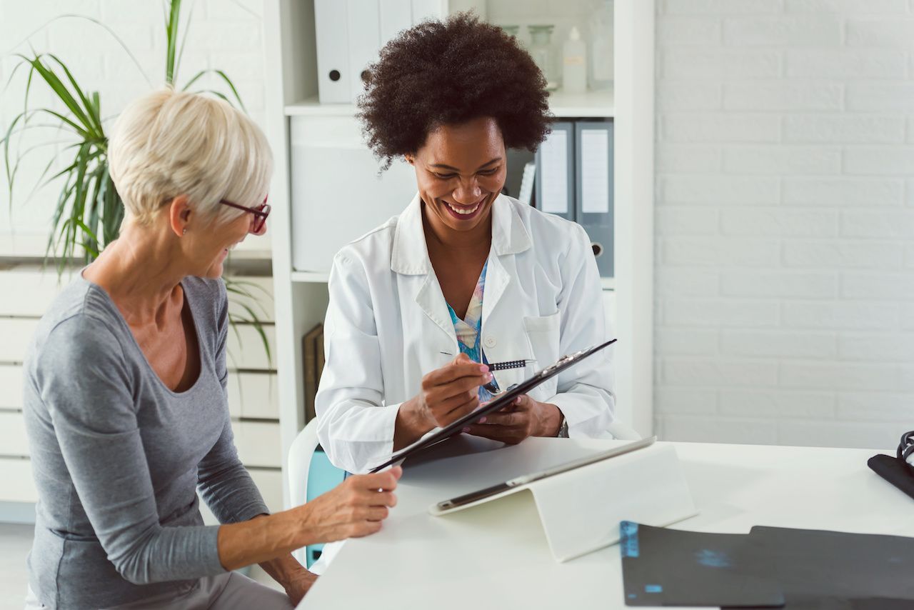 A female doctor sits at her desk and chats to an elderly female patient while looking at her test results: © lordn - stock.adobe.com