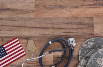 Military and Veterans Health Care Concept. Dog tags, American Flag, military camo hat and stethoscope on a wood background - Steve Cukrov - adobe.stock.com