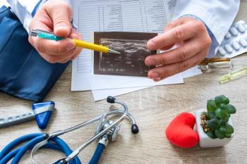 Doctor at appointment shows patient printed fragment of examination, where joint disease is recorded | shidlovski - stock.adobe.com