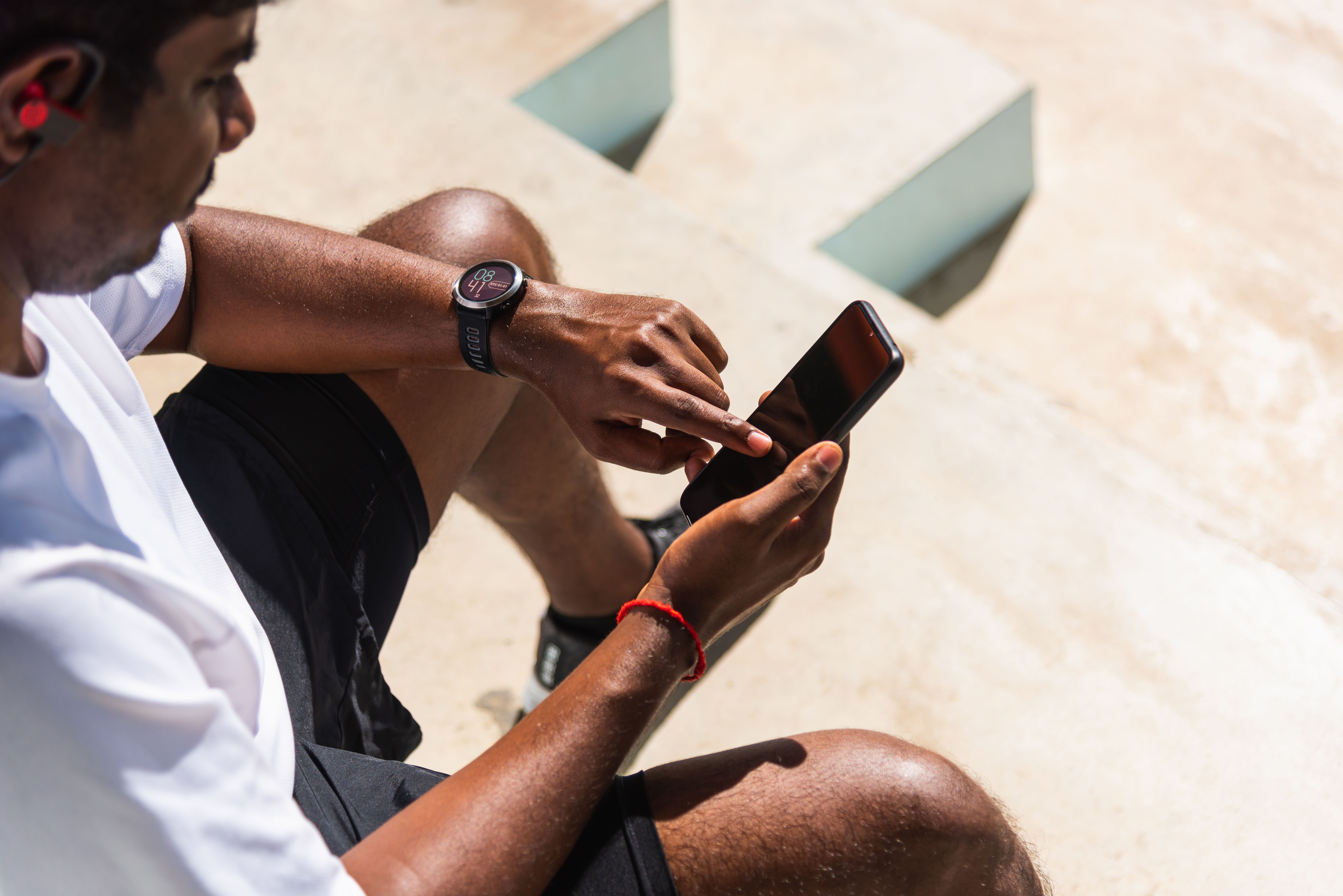 Man sitting down wearing smart watch and checking phone | Image credit: sorapop – stock.adobe.com