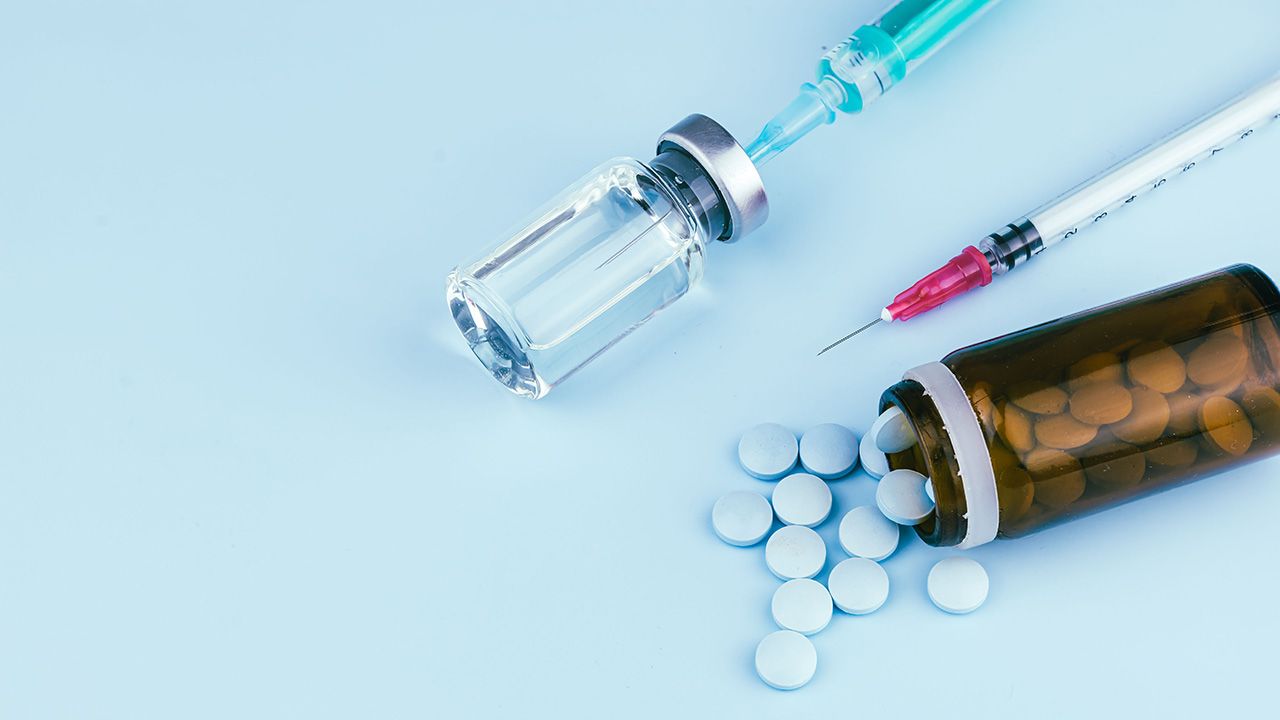 Syringe with a needle and various pills on a blue background | Image Credit: © R R/Wirestock Creators - © R R/Wirestock Creators - adobe.stock.com