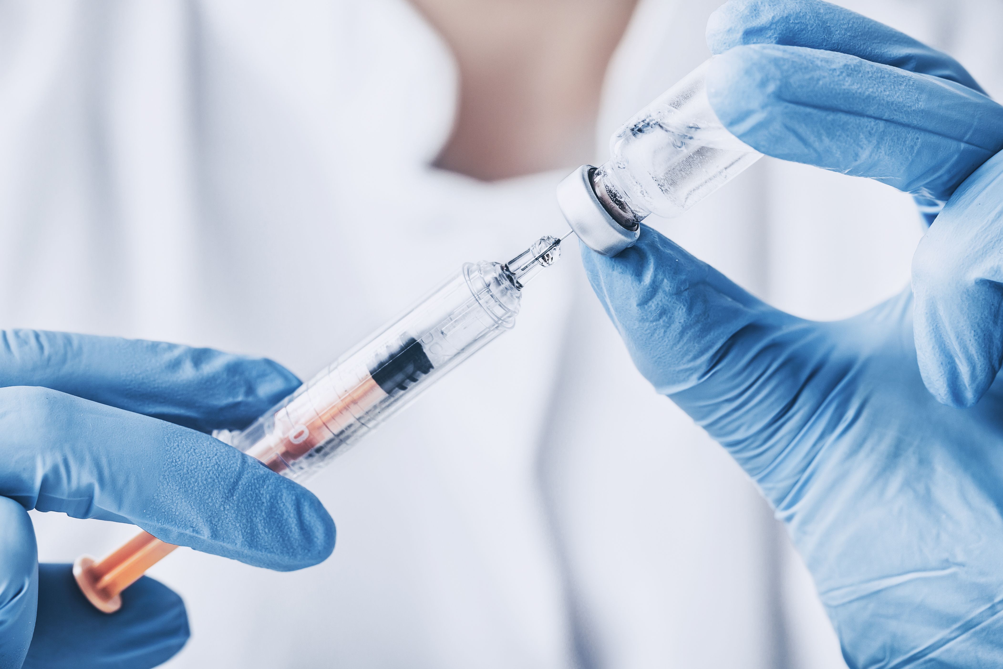Gloved hands drawing liquid from a vaccine vial into a syringe. | Image Credit: © REDPIXEL - stock.adobe.com