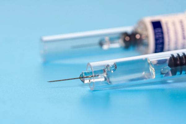 Close-up of two prefilled syringes on a light blue surface, one in focus with a clear barrel and exposed needle and a labeled syringe blurred in the background. | Image Credit: © omar - stock.adobe.com