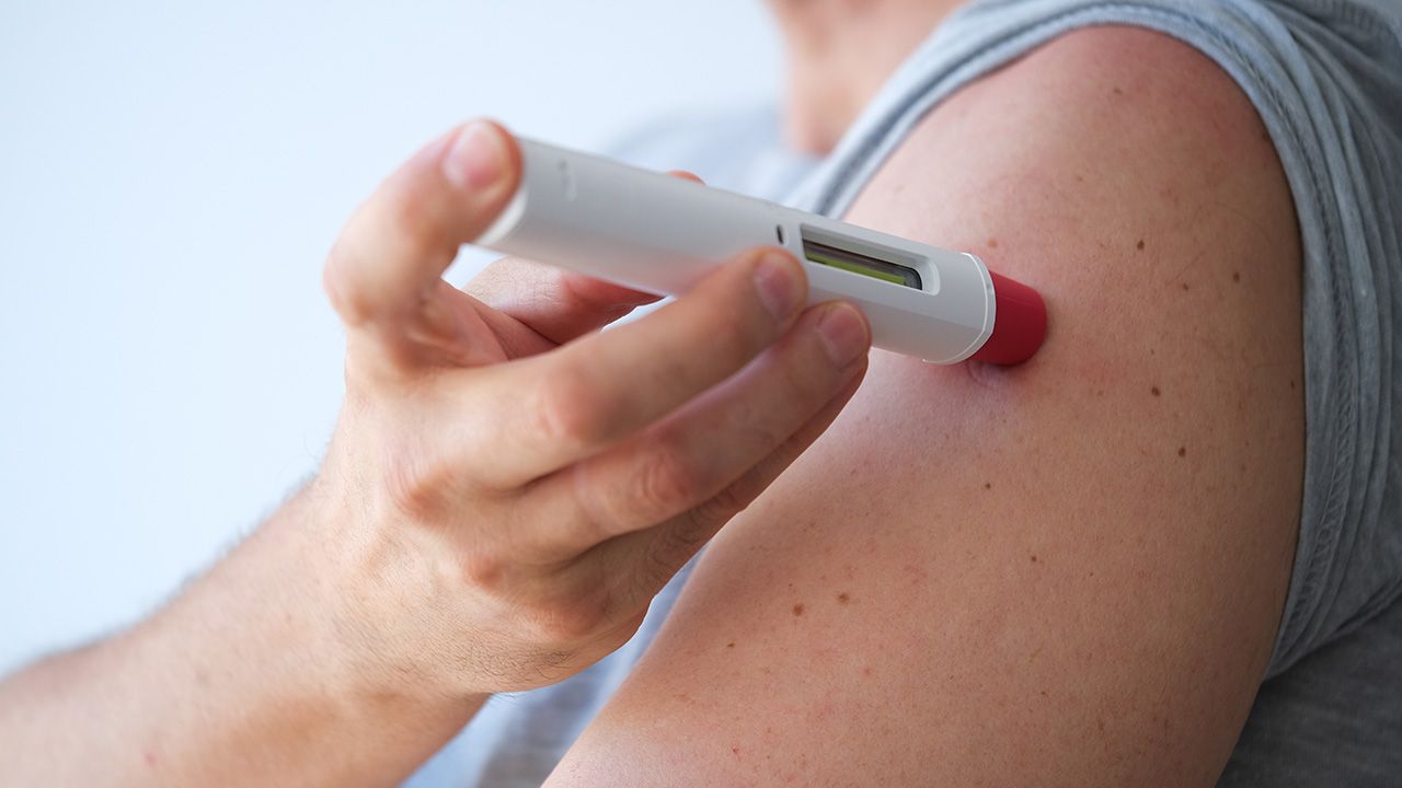 an anonymous adult man injecting himself a treatment such as insulin or Adalimumab, Etanercept or epinephrine into his shoulder. It is a white pen injector with red head for health care | Image credit: © LaMorenita - © LaMorenita - stock.adobe.com