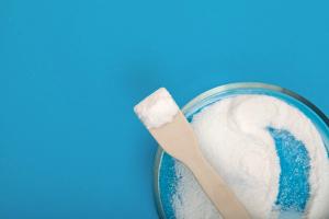 White powder in a round glass Petri dish on a blue background, with a wooden spatula resting in the dish and holding a small mound of the powder. | Image Credit: © AB-7272 - stock.adobe.com