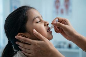 Young child receiving oral vaccine from a healthcare worker representing Shigella disease prevention in pediatric global health. | Image Credit: © Meow Creations -stock.adobe.com. 