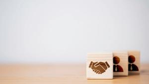 Hand shaking which print screen on wooden cube block in front of human icon for business deal and agreement concept | Image Credit: © Dilok – © Dilok - stock.adobe.com