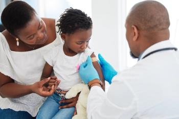 Photograph of a young girl with a bandage on her arm after receiving a vaccine, with her mother and a pediatrician present. | Image Credit: © Nina Lawrenson/peopleimages.com - stock.adobe.com