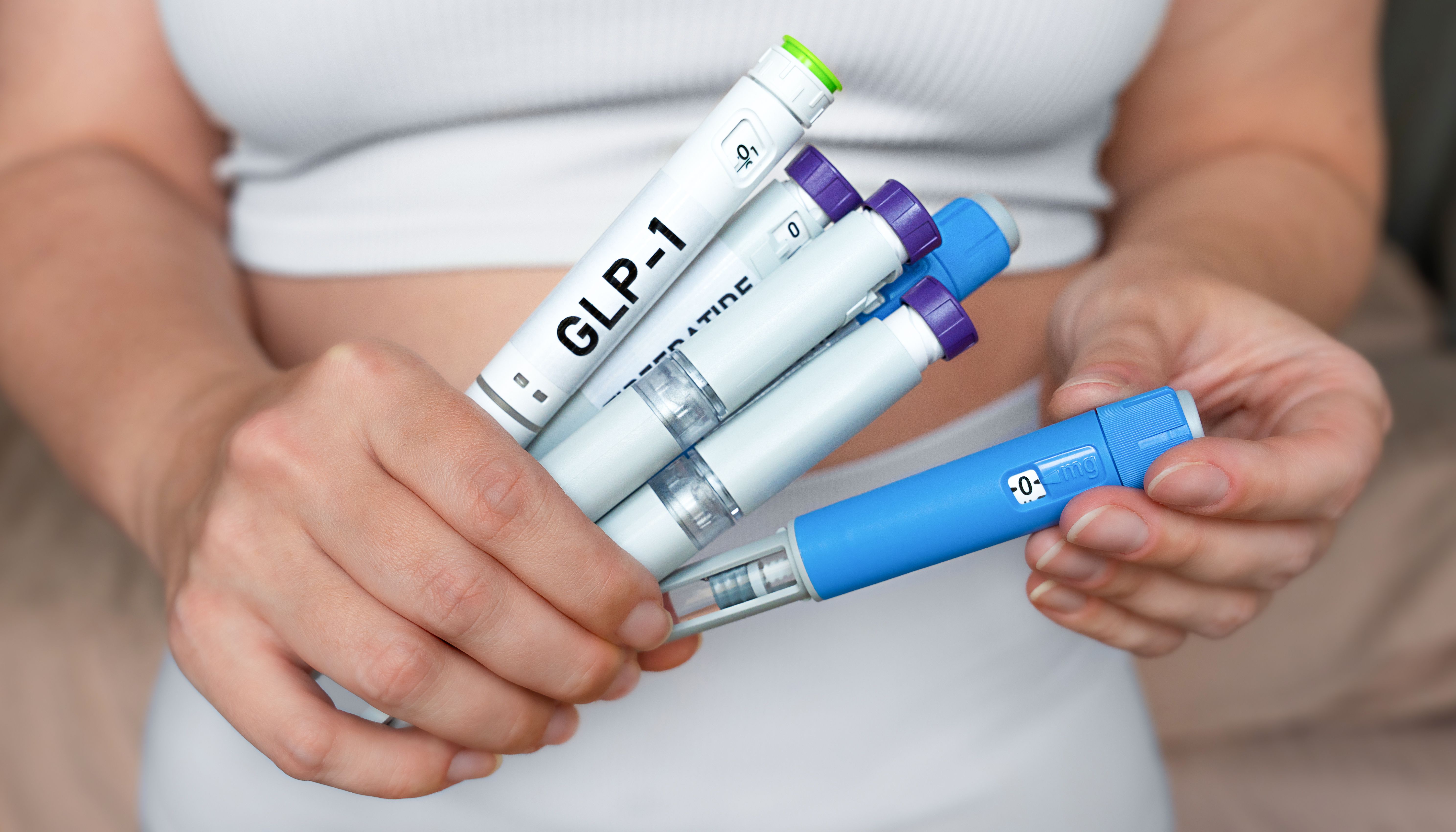 A person holding several GLP-1 injection pens. | Image Credit: © Kateryna - stock.adobe.com