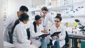 Tablet, science team and people learning for cancer cure, help or medical development in laboratory. Training, investigation or research info with scientists in clinical trial for medicine internship | Image credit: © CoetzeeRising/peopleimages.com - © CoetzeeRising/peopleimages.com - stock.adobe.com