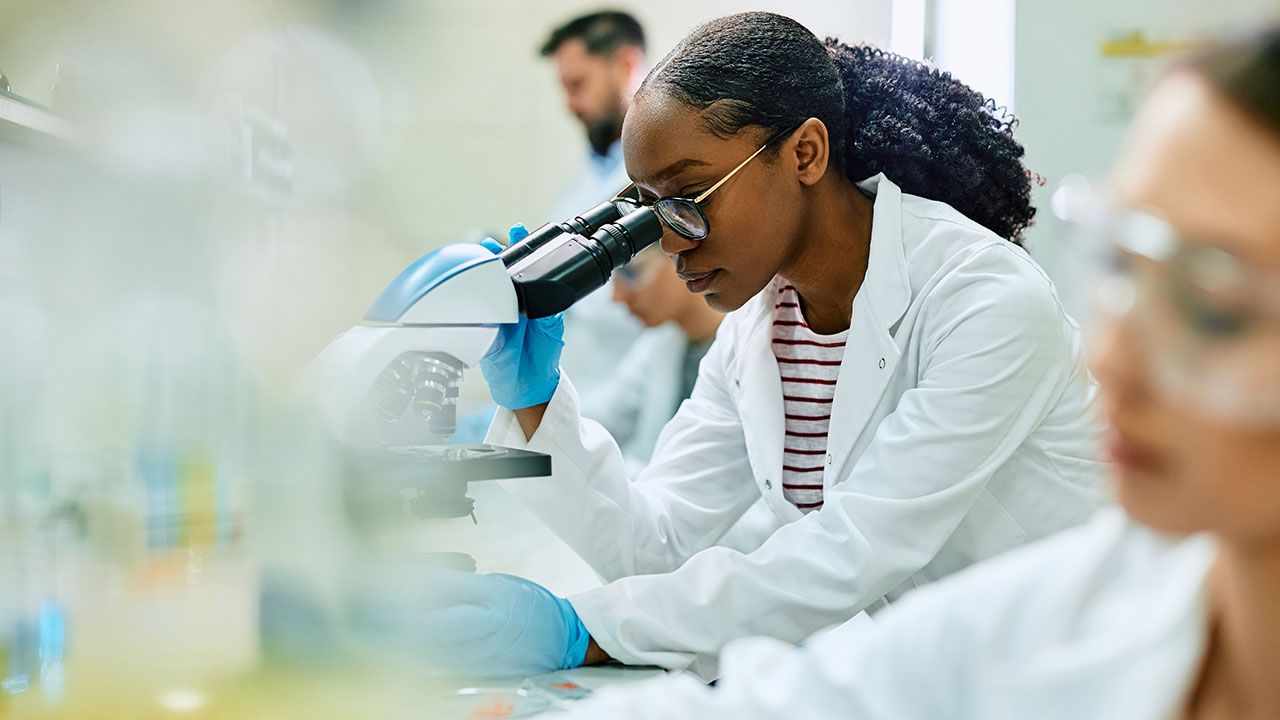 Black female scientist looking through microscope while working in laboratory. | Image Credit: ©Drazen - stock.adobe.com