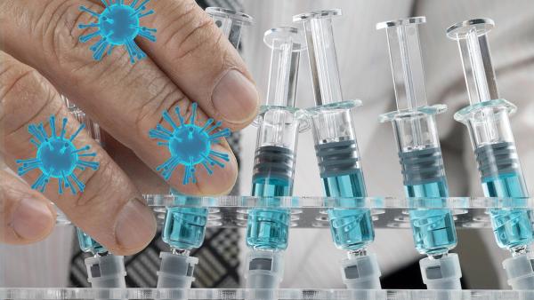 Closed up image of a doctor holding a glass syringe with several other syringes prefilled with blue liquid on a rack. Covid-19 vaccination concepts. | Image credit: © SOPONE - © SOPONE - stock.adobe.com