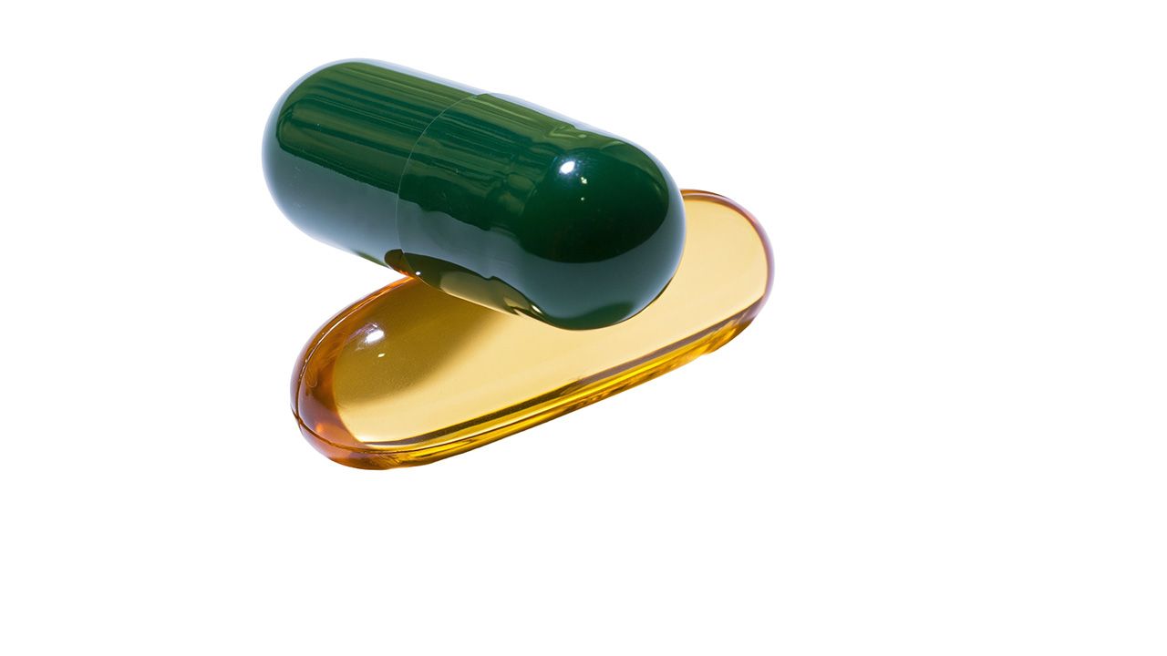 Green gelatin capsule resting on a translucent amber liquid drop, isolated on transparent background | Image credit: © Nina - © Nina - stock.adobe.com