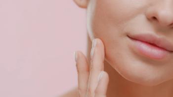 Extreme close-up shot of attractive young slim white-skinned woman strokes her jawline smiling for the camera on pale pink background. | Image Credit: © pavel_dp - stock.adobe.com