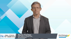 Nuno Fontes, man in black suit jacket and white button down standing in front of blue and white background for interview