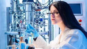 Laboratory assistant works next to the bioreactor. Concept - woman synthesizes a bio preparation. Vaccine development. Girl works as a biologist. Woman works as a pharmacologist. Scientific research | Image Credit: ©Grispb - stock.adobe.com