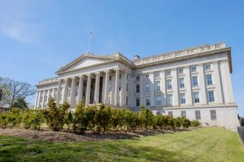 Exterior of the US Department of the Treasury building in Washington, DC, with a columned entrance, an American flag on the roof, green shrubs and a lawn in the foreground, and a clear blue sky. | Image Credit: © Jorge Moro - stock.adobe.com