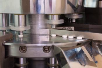 Tablet press machine producing white tablets. | Image Credit: © Dr.Bakl - stock.adobe.com