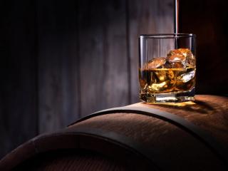 Glass of whiskey with ice cubes on the wooden barrel with wooden background. | Image Credit: © Alexandr Steblovskiy - stock.adobe.com.