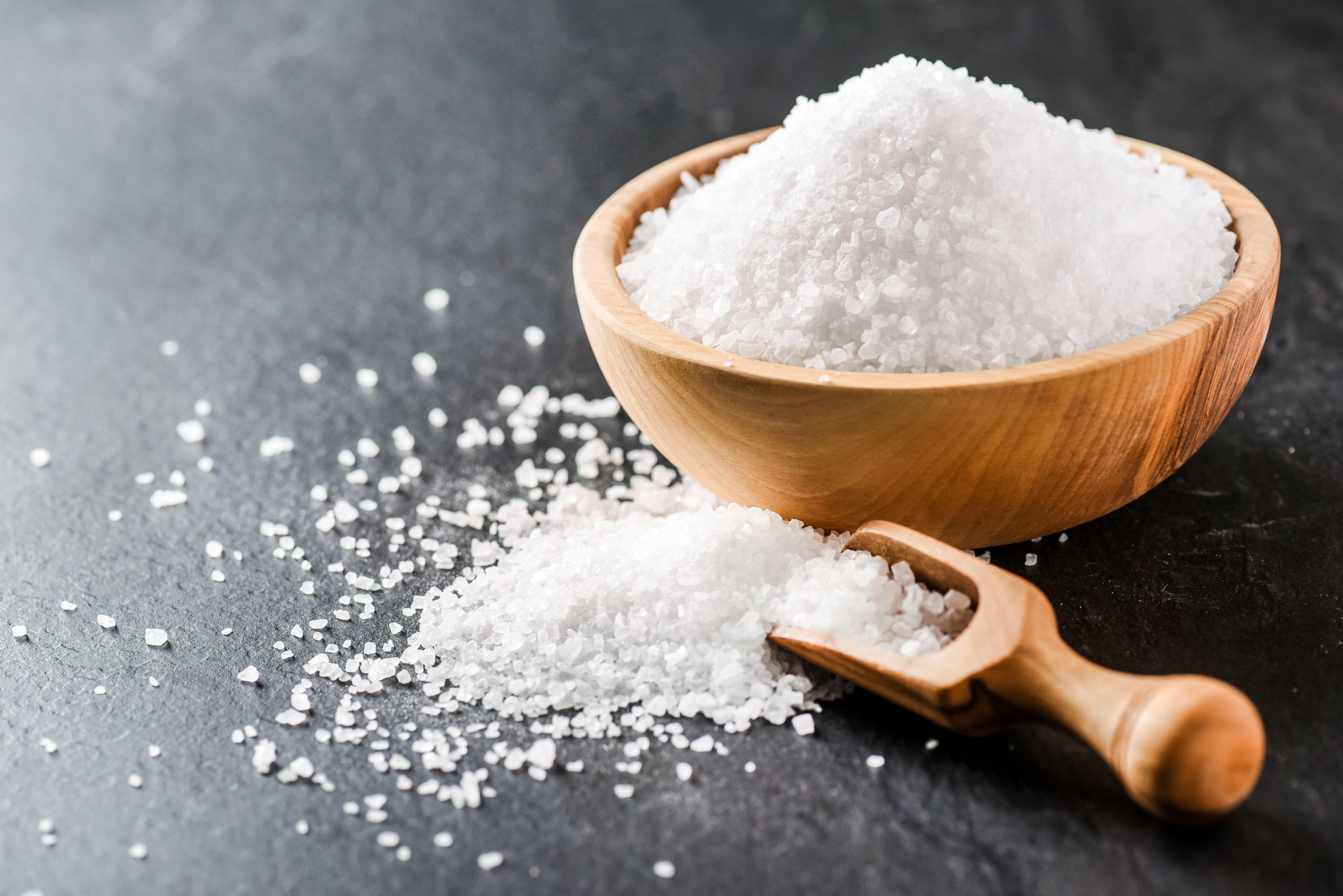 Salt in wooden bowl on dark stone table. Sea salt on black background. | Image Credit: © Milan - stock.adobe.com