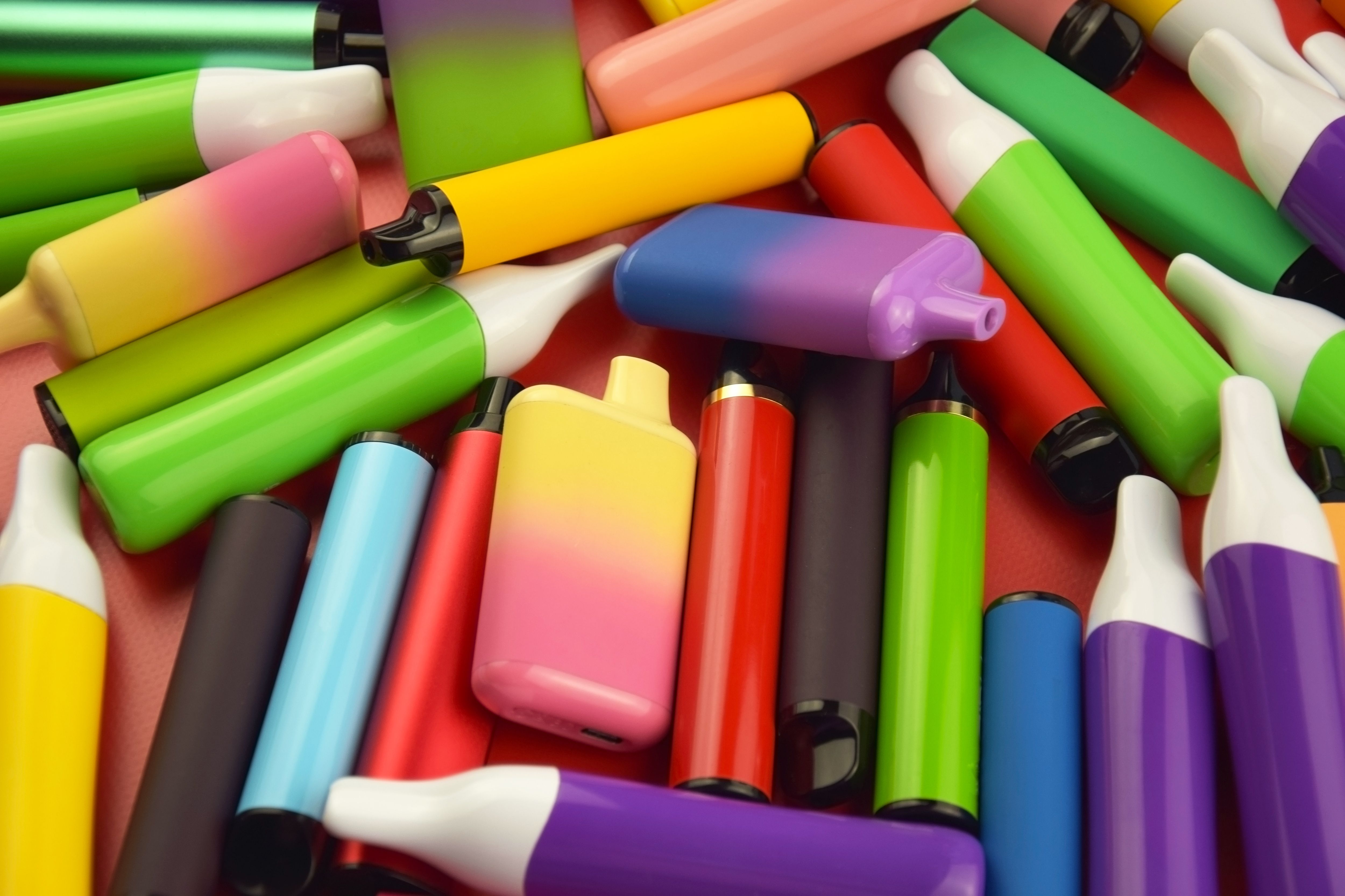 Set of multicolor disposable electronic cigarettes on a red background. | Image Credit: © iama_sing - stock.adobe.com