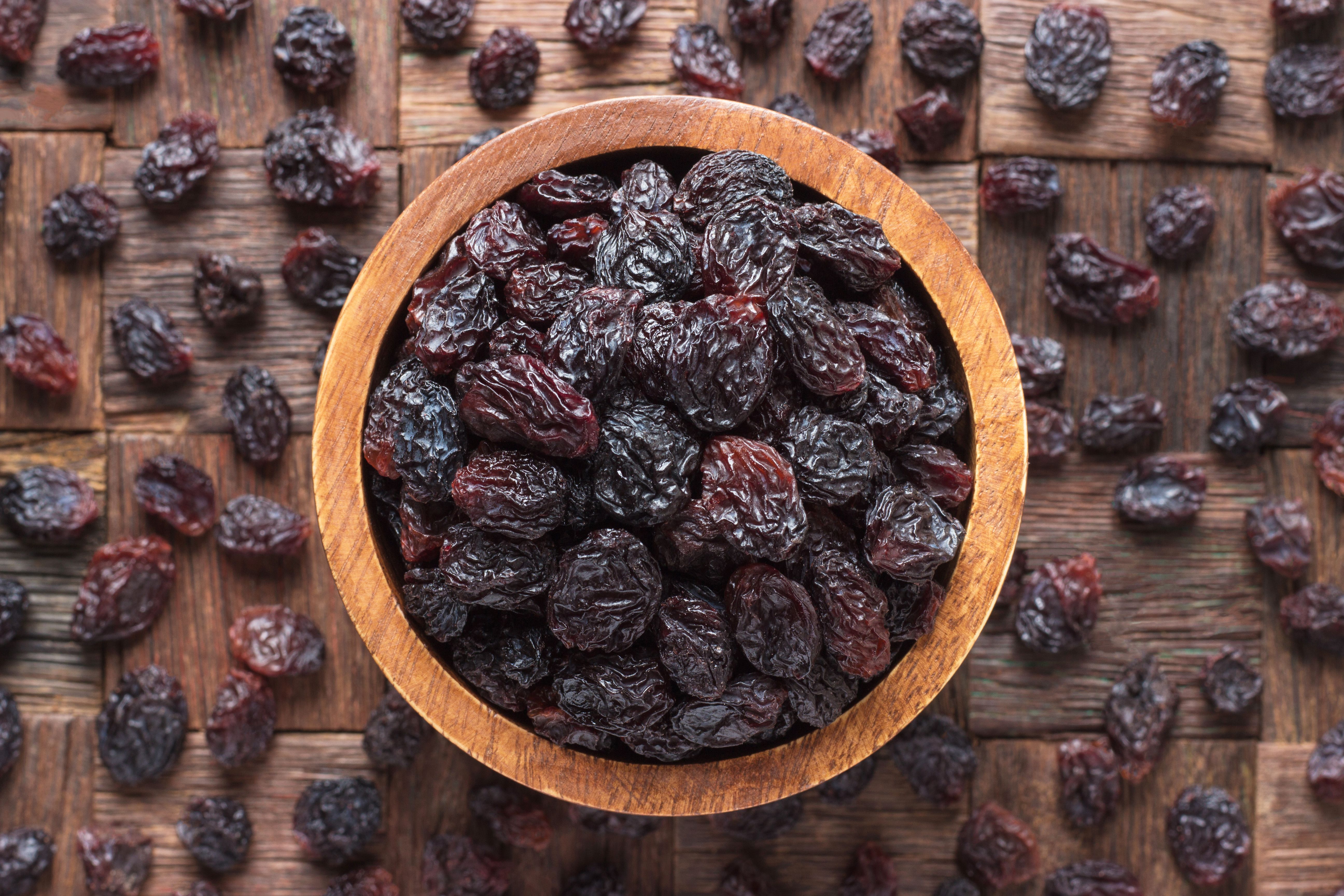 Dried grapes, dark raisins in wooden bowl, top view. | Image Credit: © dmitr1ch - stock.adobe.com