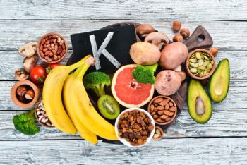 Foods containing natural potassium. K: Potatoes, mushrooms, banana, tomatoes, nuts, beans, broccoli, avocados. Top view. On a white wooden background. | Image Credit: © Yaruniv-Studio