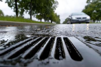 Close-up of storm drain during rainfall, car driving in background on wet road. © Moopingz - stock.adobe.com