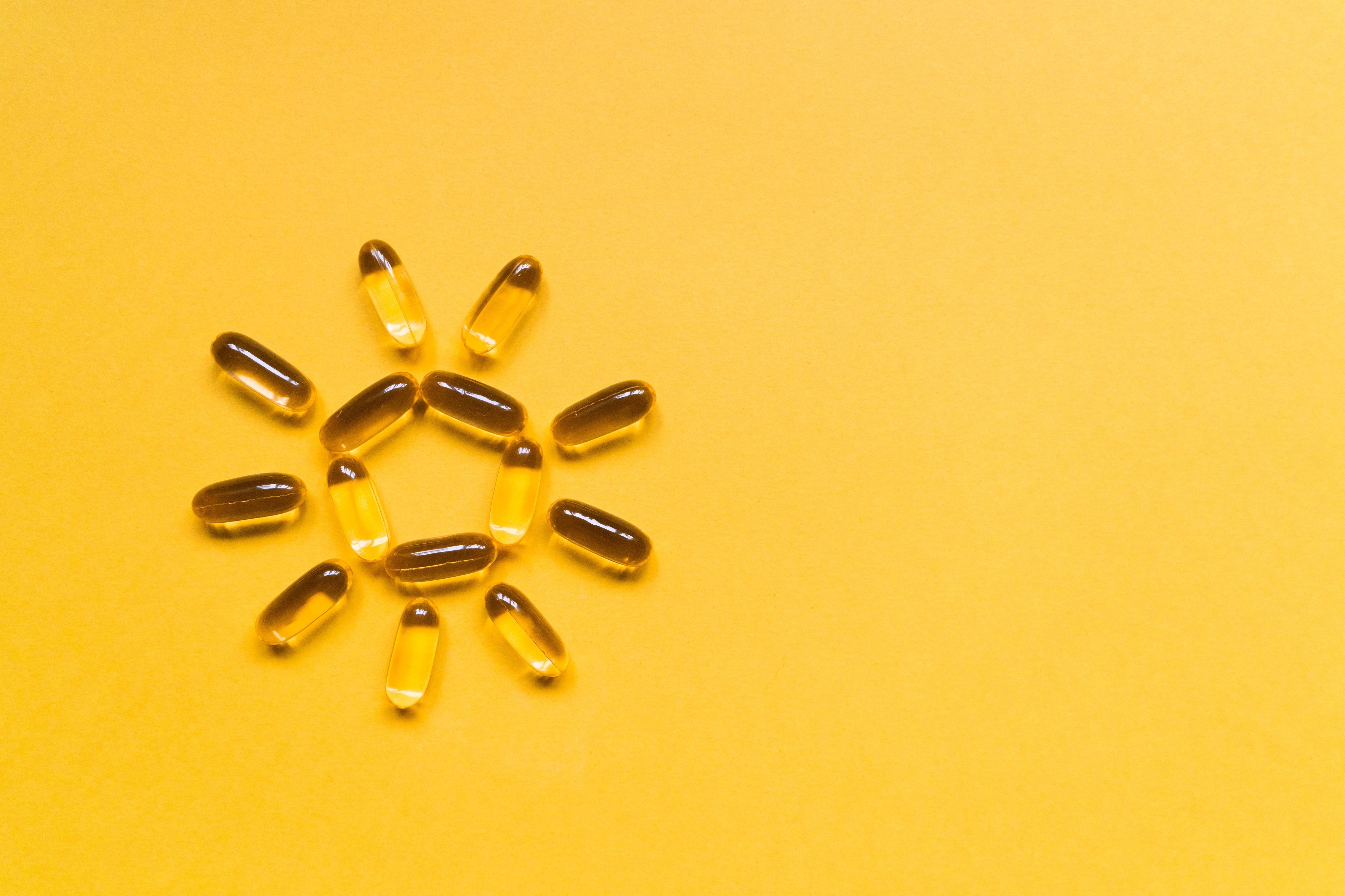 Close up capsules of fish fat oil in the sun shape, omega 3, vitamin e on the yellow background. Healthy food diet. Nutritional supplement | Image Credit: © MagicalKrew - stock.adobe.com