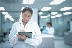 A confident young female scientist in a lab coat and goggles stands with arms crossed in a modern laboratory, representing the bright future of women in STEM careers and research. | Image Credit: © ultramansk - stock.adobe.com.