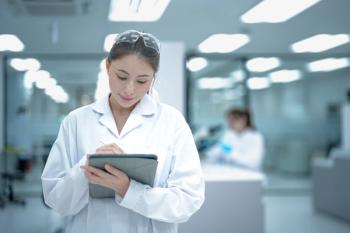 A confident young female scientist in a lab coat and goggles stands with arms crossed in a modern laboratory, representing the bright future of women in STEM careers and research. | Image Credit: © ultramansk - stock.adobe.com.