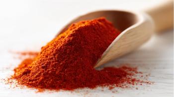 Close-up of vibrant red chili powder in wooden scoop on white surface with loose powder scattered. | Image Credit: © AI Images - stock.adobe.com.