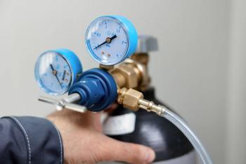 A metrology laboratory specialist takes a compressed gas cylinder for testing and calibration with a chromatograph. A man connects a hose for gas analysis. Gas analyzer and chromatography. | Image Credit: © NEZNAEV