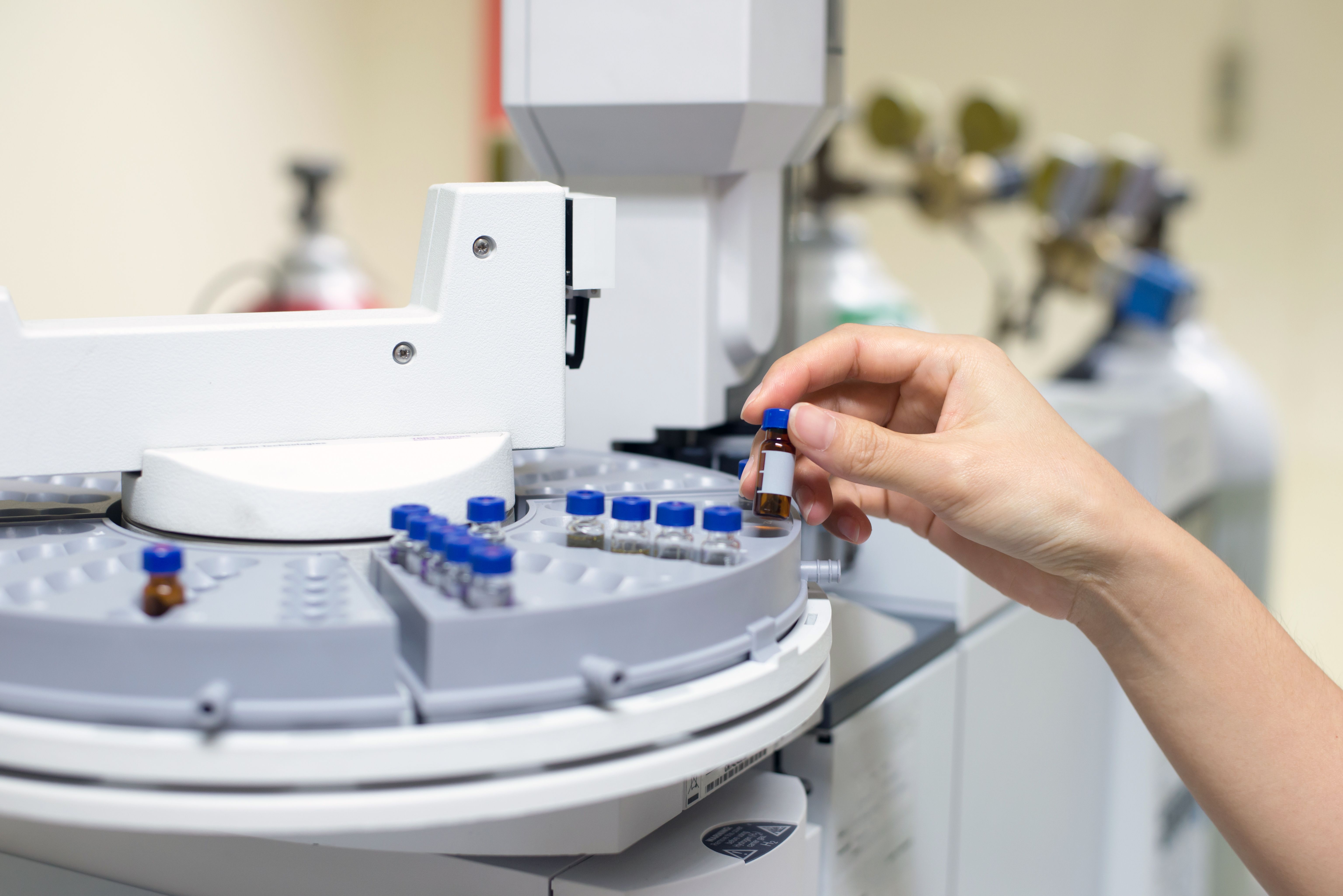 Scientist hand holding an amber vial, Vials in the autosampler tray. Chemistry lab | Image Credit: © bigy9950 - stock.adobe.com