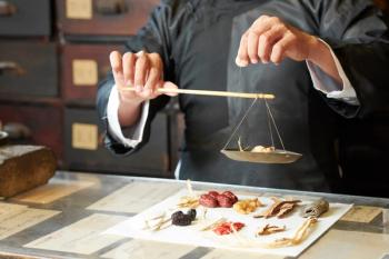 Close-up image of traditional Chinese medicine practitioner using special scales to weight dry plant roots for treatment | Image Credit: © DragonImages - stock.adobe.com