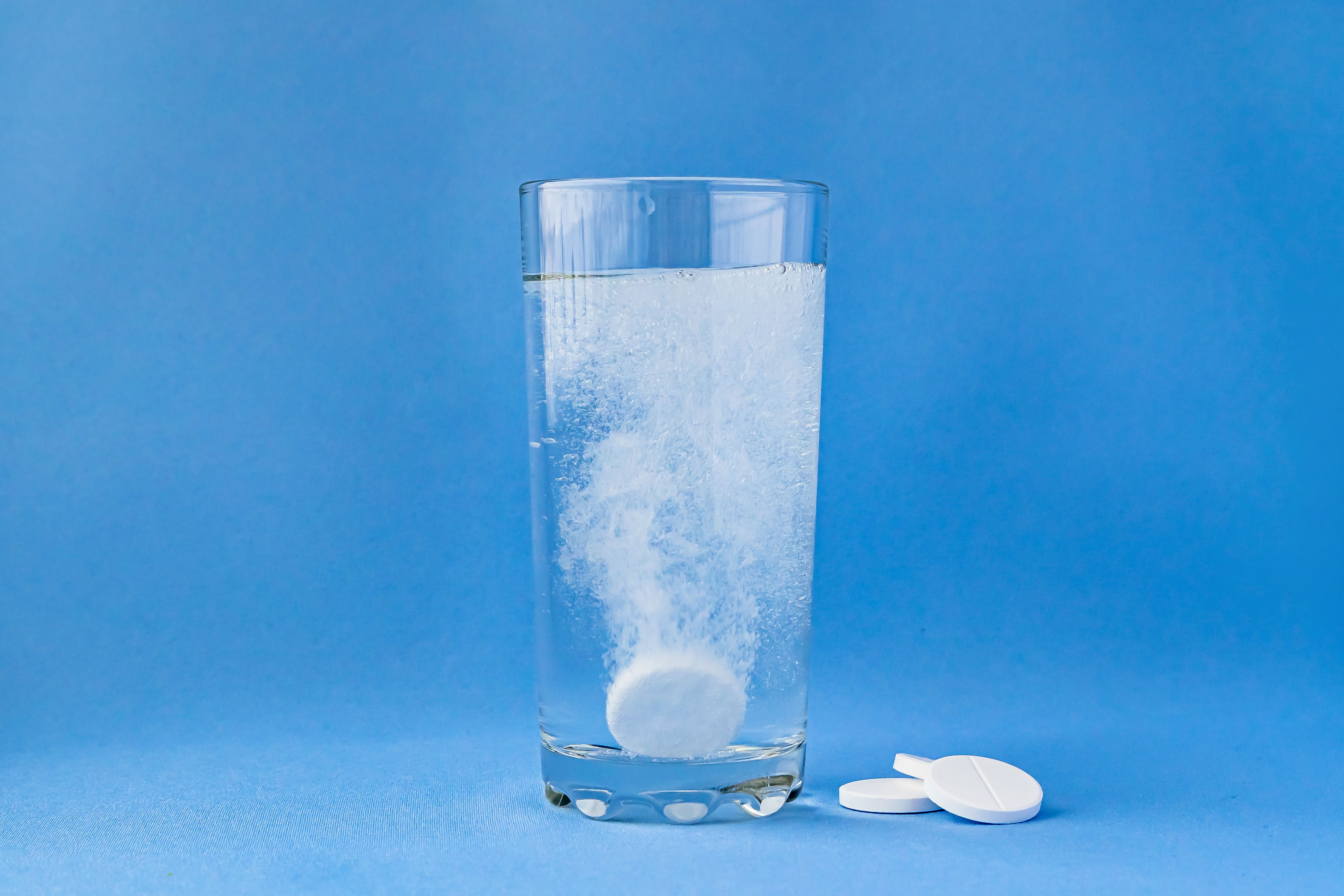 Fizzy aspirin in a glass of water on a blue background. Vertical format and soft focus. | Image Credit: © Natalia - stock.adobe.com
