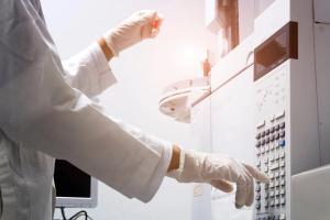 scientist holds an amber vial and press the control button of GC chromatography | Image Credit: © Anchalee - stock.adobe.com.
