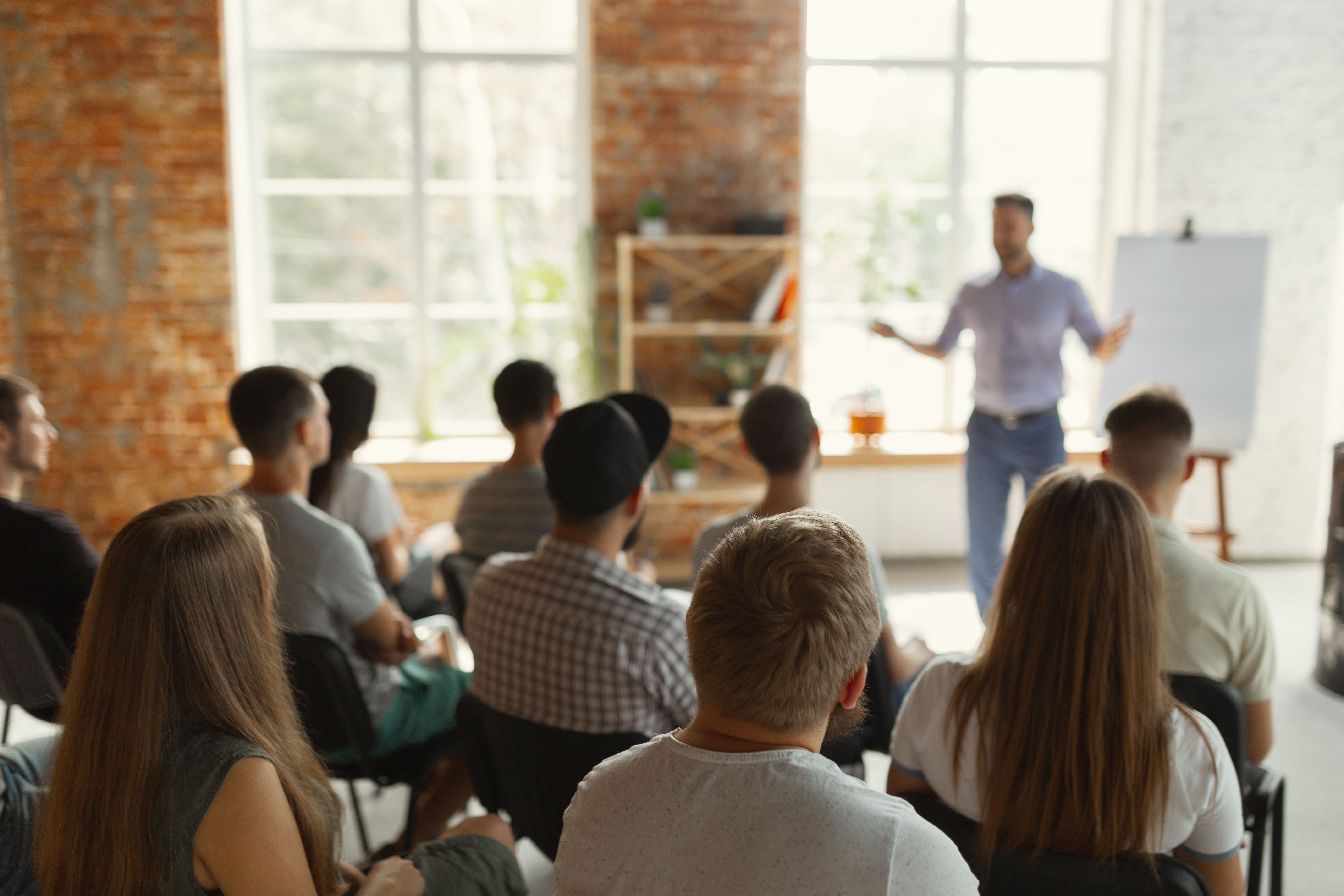 Male speaker giving presentation in hall at university workshop. Audience or conference hall. Rear view of unrecognized participants in audience. Scientific conference event, training. Education | Image Credit: © master1305 - stock.adobe.com