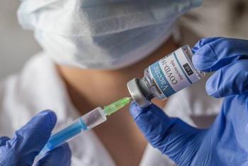 clinician wearing face mask and gloves holds bottle for injection of covid-19 vaccine with syringe