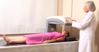 Female doctor examining woman in 40s at Bone Densitometer Machine.
