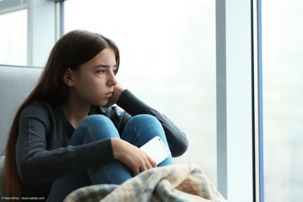 Upset teenage girl with smartphone sitting at window indoors. Space for text | Image Credit: © New Africa – stock.adobe.com