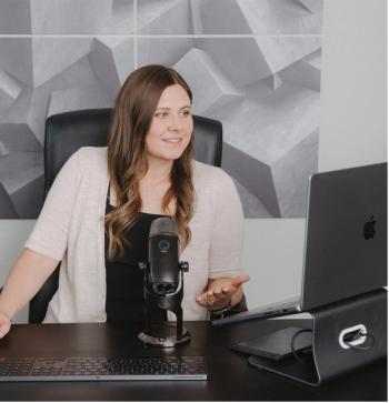 Cancer survivor and podcaster, Katie Coleman, speaking into a microphone and looking at her computer| Photo credit: Zach Brigham