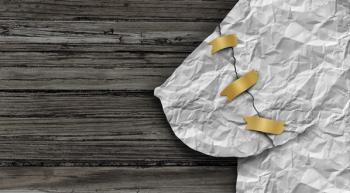 Image of a wooden background with a paper breast being held together with three pieces of tape.
