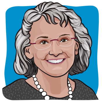 A woman with short gray hair with glasses wearing a black polka dot blouse with a pearl necklace.