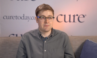 A man with a dark gray button-up shirt with glasses and cropped brown hair.