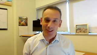 Image of a man with short hair, wearing a buttoned-up shirt.